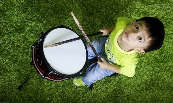 Kleiner Junge schaut nach oben und hält zwei Schläger für eine Trommel in den Händen.