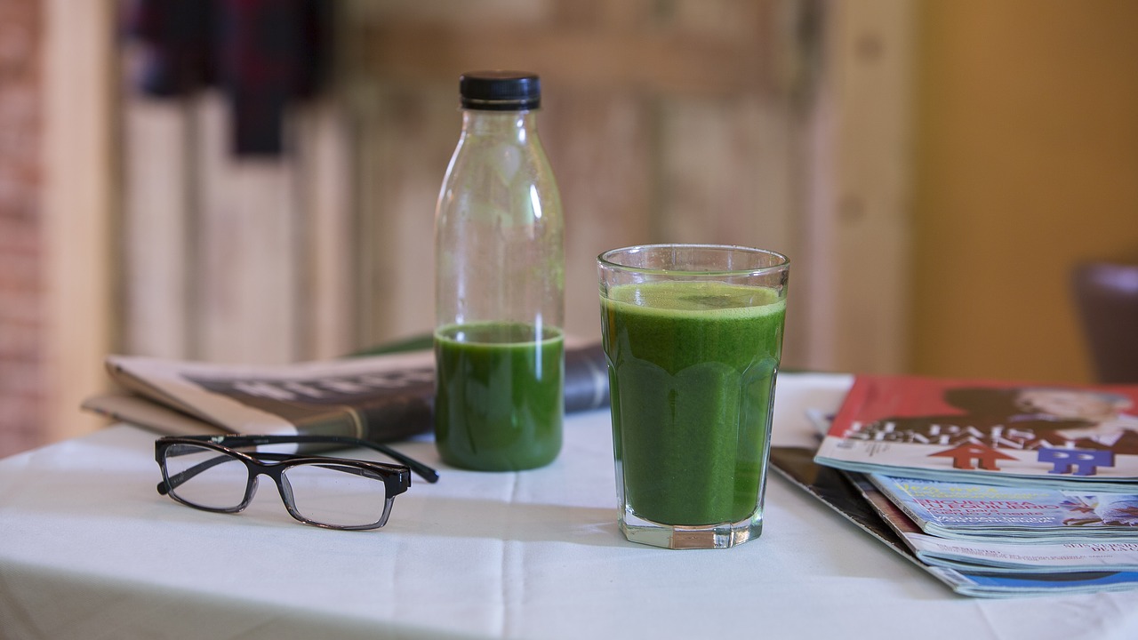 Superfood Sellerie - Auf dem Bild ist ein Glas und eine Flasche mit Smoothie zu sehen, links daneben liegt eine schwarze Brille und rechts daneben ein Stapel Zeitschriften. Im Hintergrund eine Zeitung.