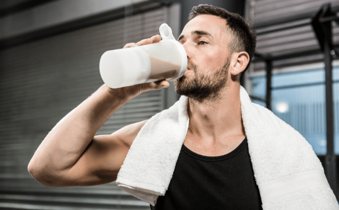 Ein trainierter Mann trinkt einen Proteinshake im Fitnessstudio