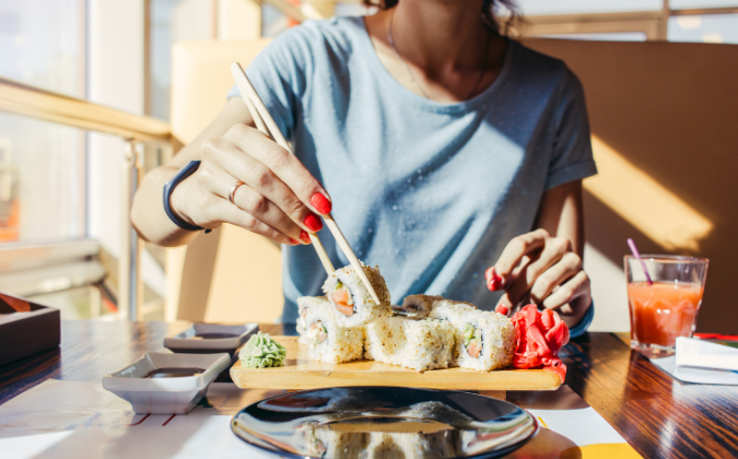 Eine Frau sitzt in einem Sushi-Restaurant und isst Sushi mit Stäbchen