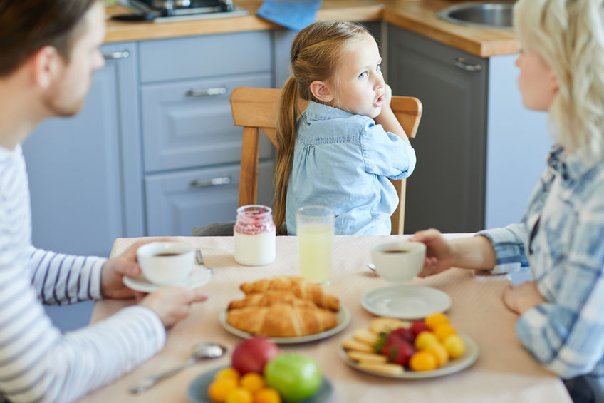 Eine Familie sitzt am Frühstückstisch und die Tochter dreht sich vom Tisch weg.