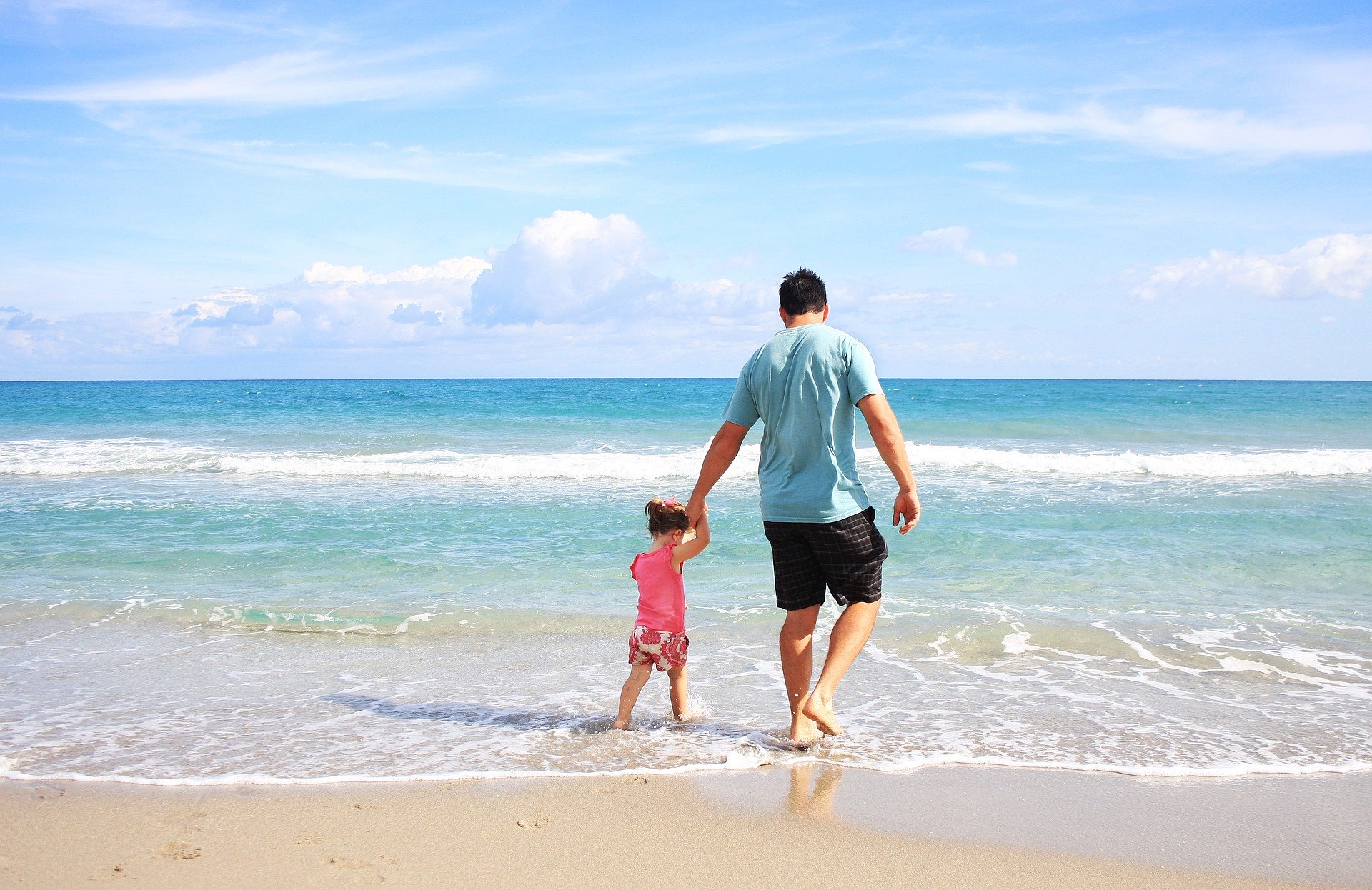 Vater hält Tochter an der Hand und sie laufen am Strand entlang.