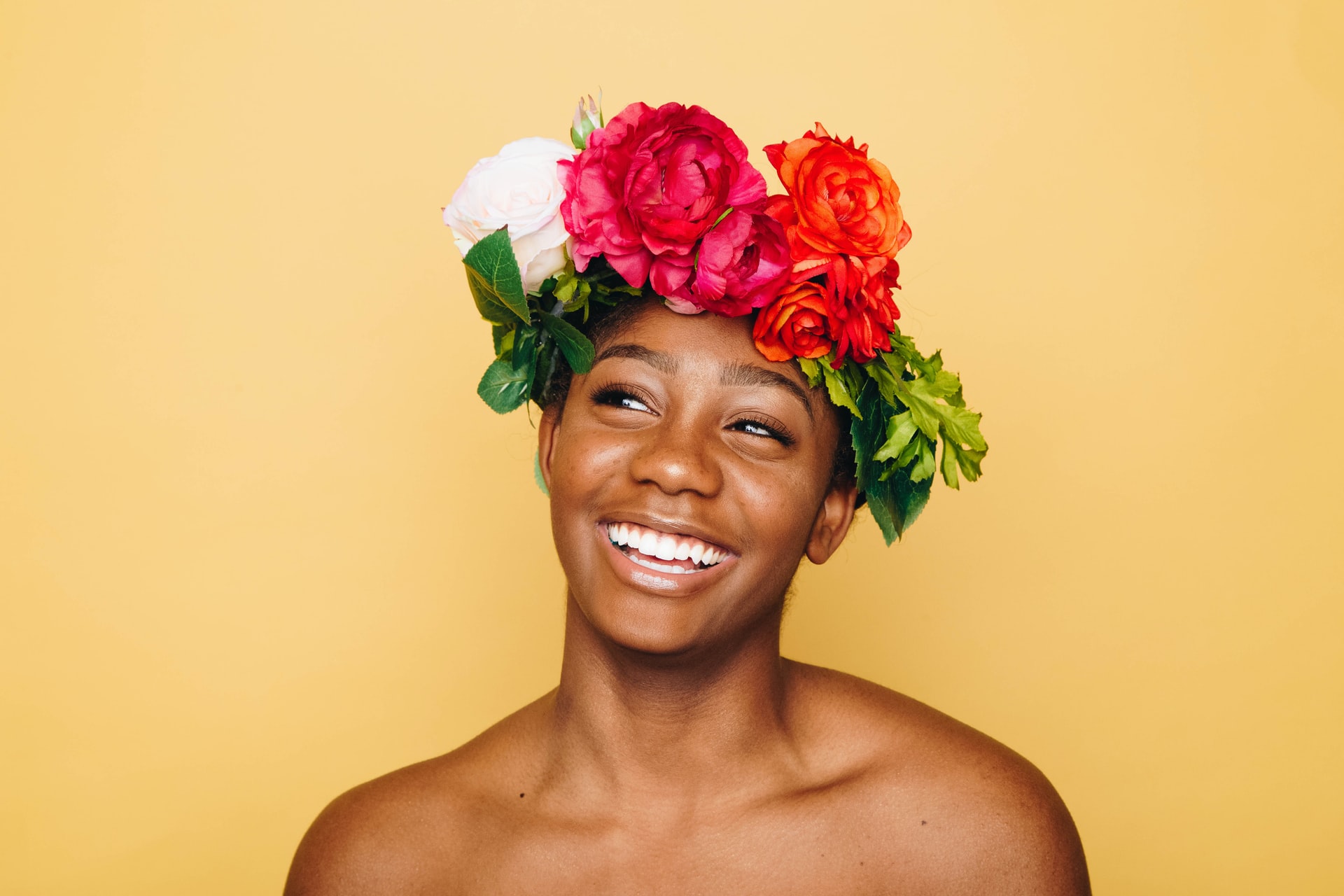 Eine Frau trägt einen bunten Blumenkranz auf dem Kopf, schaut zur Seite und grinst.