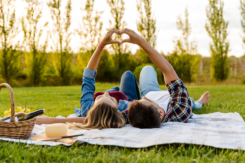 Ein Paar liegt in einem Park auf einer Picknickdecke und formt die Hände zu einem Herz.