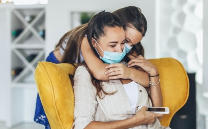 Spuren der Corona-Pandemie | apomio Gesundheitsblog | Schwestern umarmen sich fröhlich und tragen dabei Masken