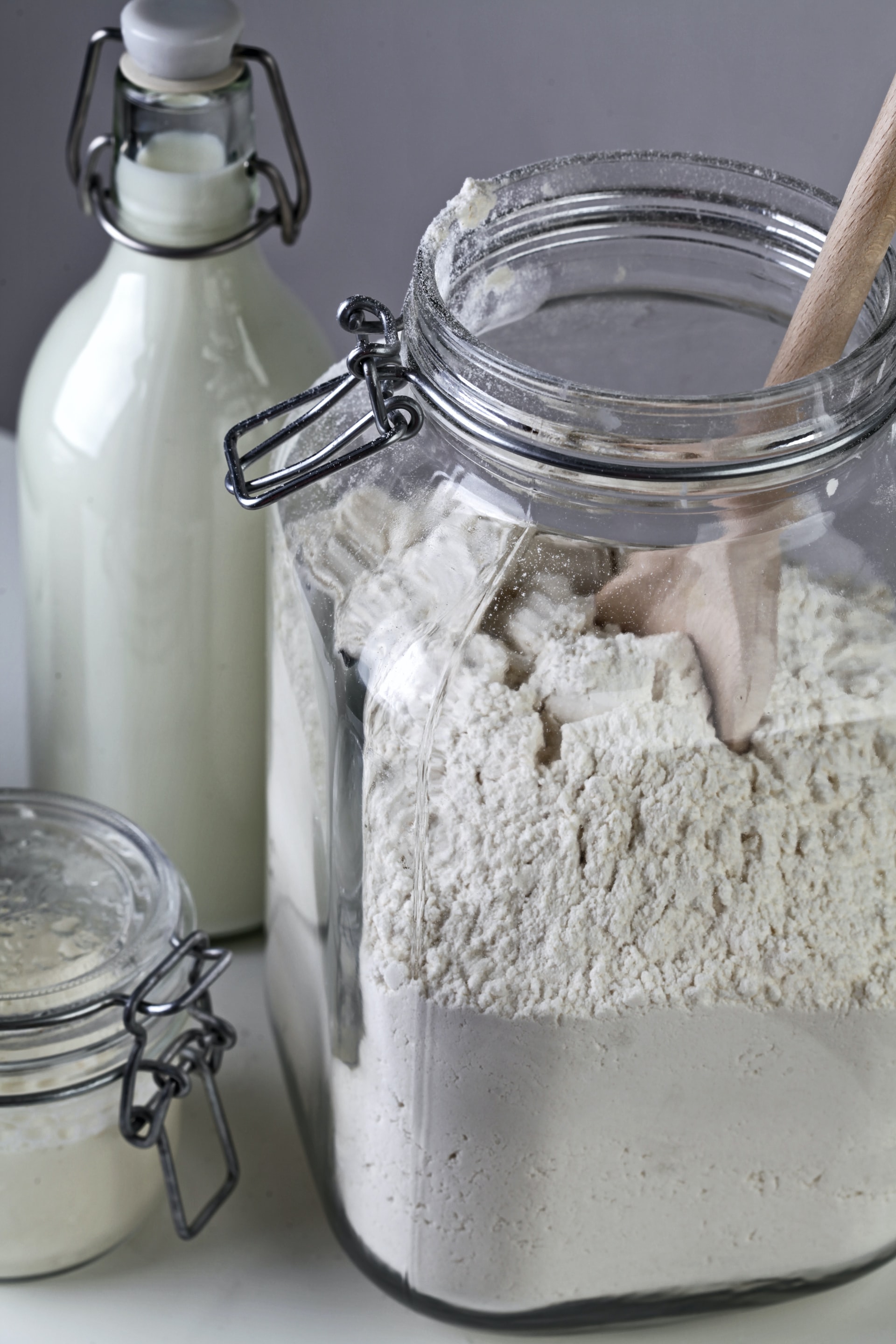 Mehlsorten - Welche Unterschiede gibt es? Auf dem Bild ist ein Gefäß mit Mehl und einem Holzlöffel zu sehen. Dahinter eine Flasche Milch.