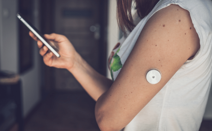 Eine Frau trägt einen Diabetes Sensor an ihrem Arm und beobachtet die Daten im Smartphone aus