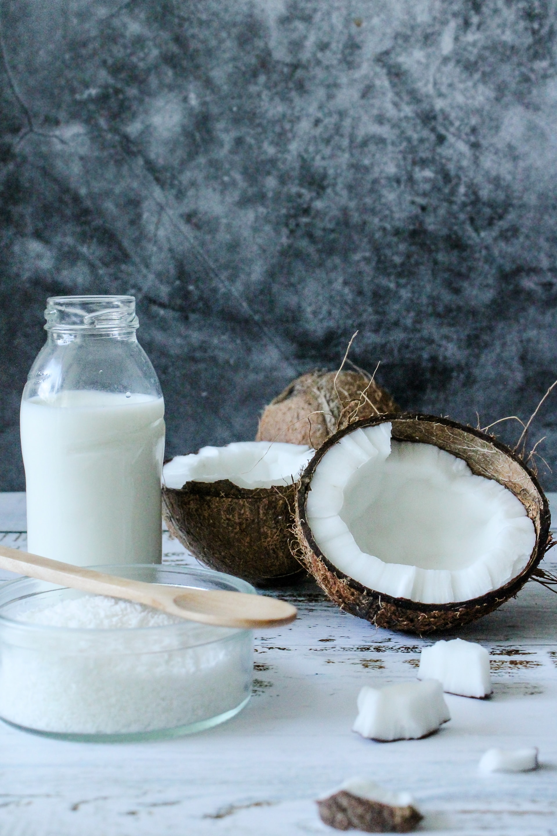 Mehlsorten - Welche Unterschiede gibt es? Auf dem Bild ist eine halbierte Kokosnuss zu sehen. Links daneben eine Flasche mit Milch und davor eine Schüssel mit Mehl und einem Holzlöffel.