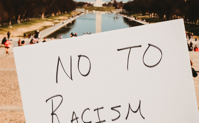 Auswirkungen von Rassismus auf die physische und psychische Gesundheit | apomio Gesundheitsblog | Schild mit der Aufschrift "No to Racism"